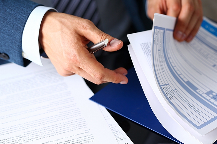 man hands insurance form clipped to pad and silver pen to sign