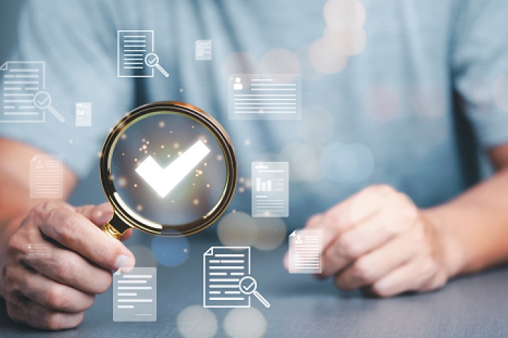 Hands holding a magnifying glass highlighting a checkmark symbol, surrounded by digital document icons.