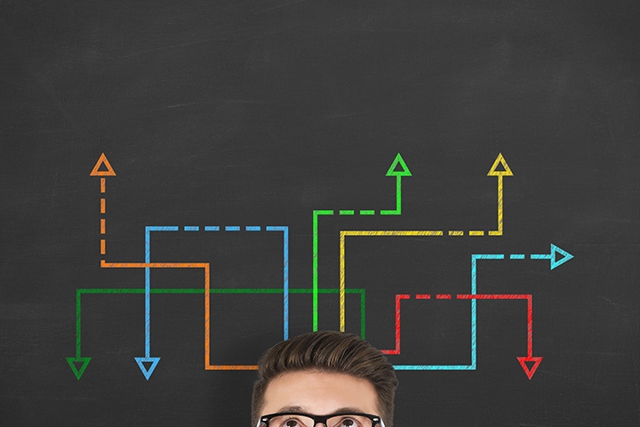 young businessman looking at many twisted arrows on the blackboard background
