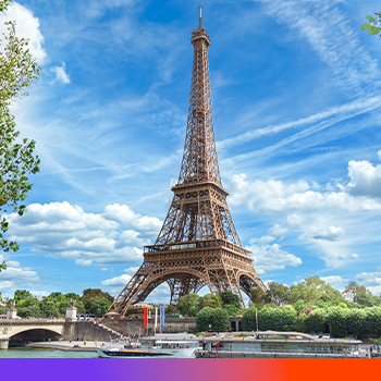 Eiffel Tower in Paris with blue sky, white clouds, green trees, and Seine River with boat in foreground.