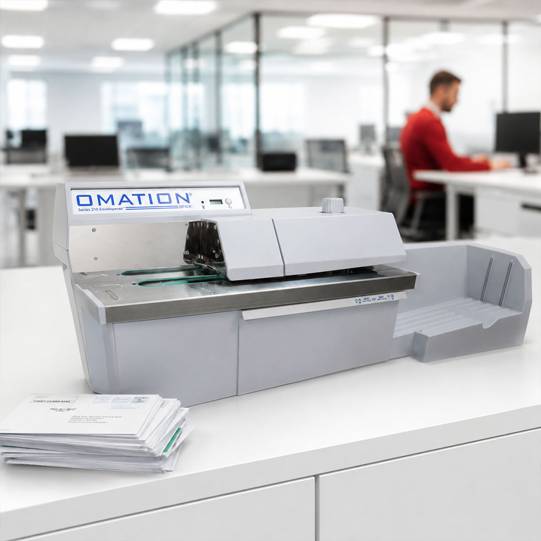 White Omation Series 210 envelope sealer machine on office desk with stack of envelopes and person in red shirt working.
