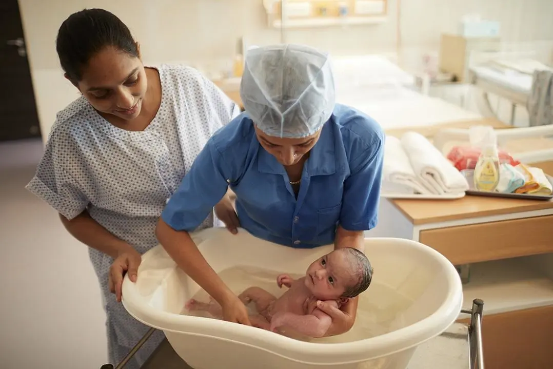 Duas mulheres dando banho num bebê na banheira