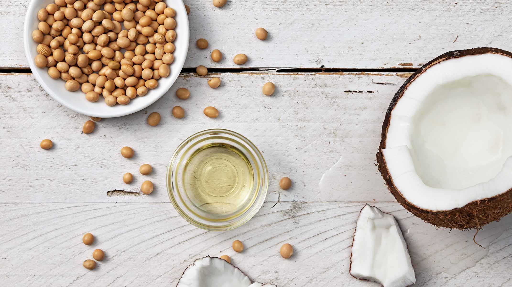 Metade de um coco na mesa, juntamente de óleo e soja num recipiente