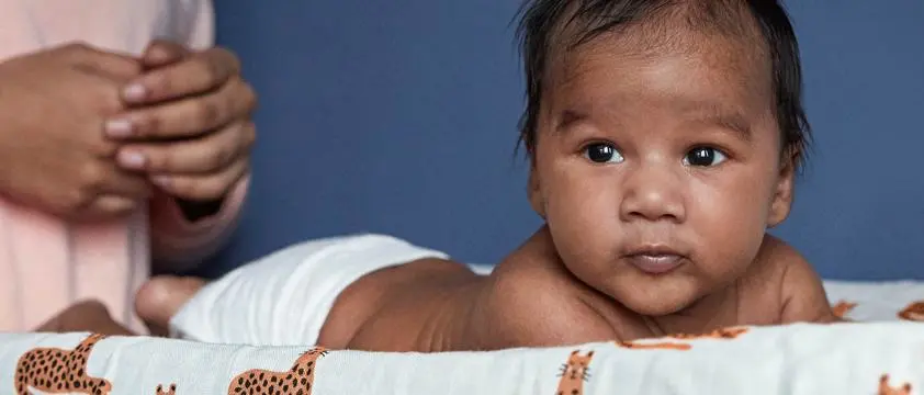 Bebê deitado de bruço no trocador, olhando para o lado