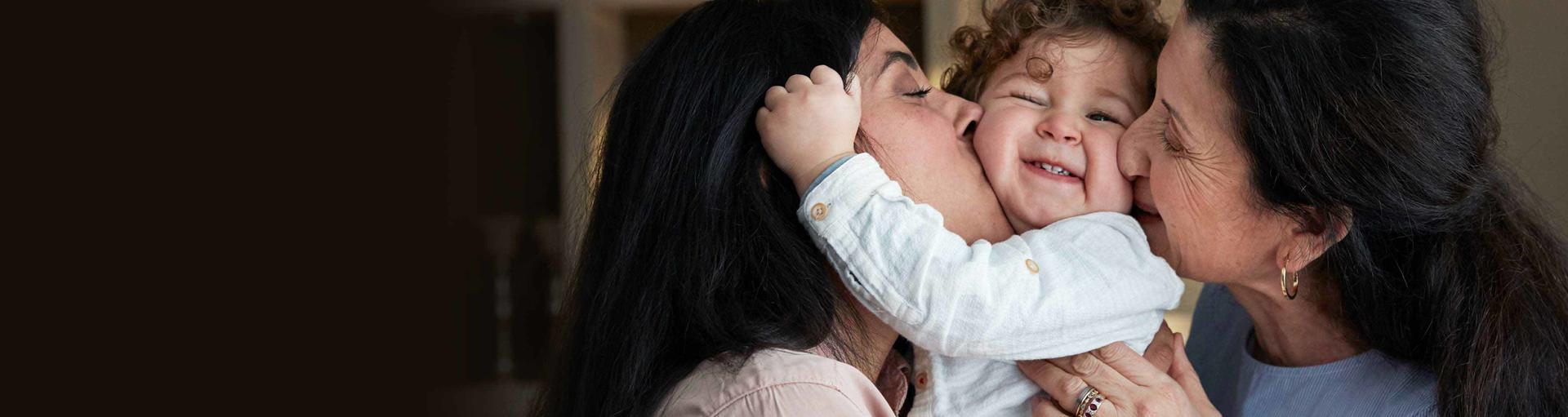 Mulher e senhora abraçando um bebê sorridente