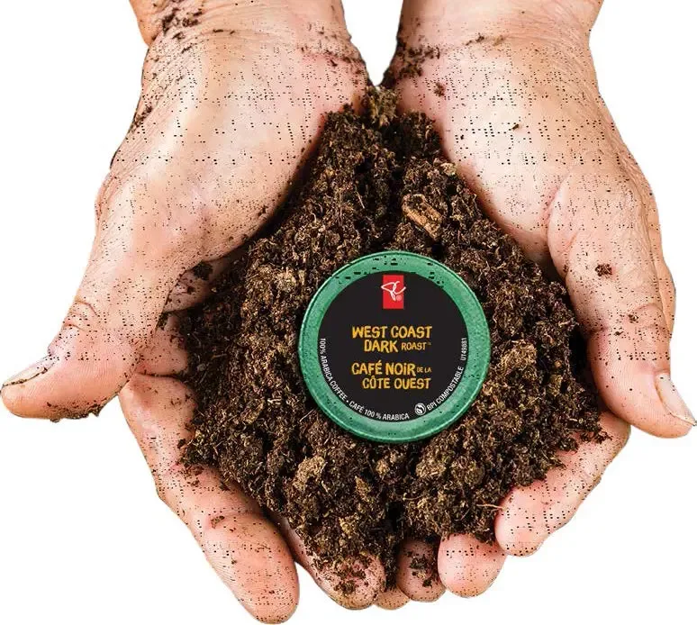 A person holding soil in their hands with a dark roast coffee cup in the center