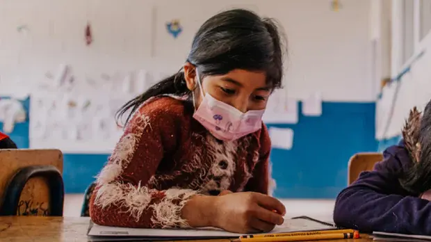 Child wearing a mask and drawing in a book