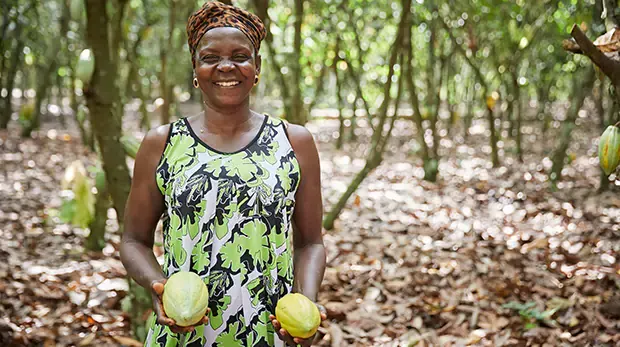 A woman smiling holding two cocoa beans
