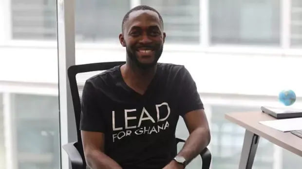 A smiling man sitting on a chair in an office area