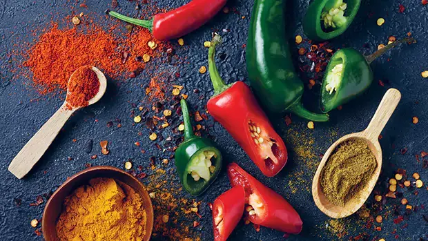 Flat lay of green and red jalapenos with various spices on the side