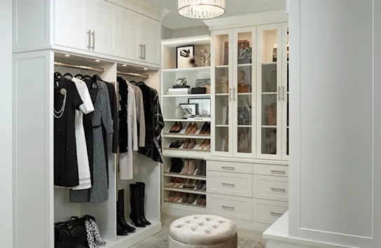 Image of a traditional style custom walk-in closet design with white Shaker cabinets, shoe shelves, built-in lighting. crown molding and other accessories