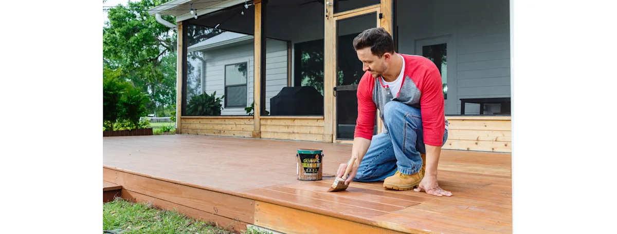 A carpenter painting a sealer onto a deck