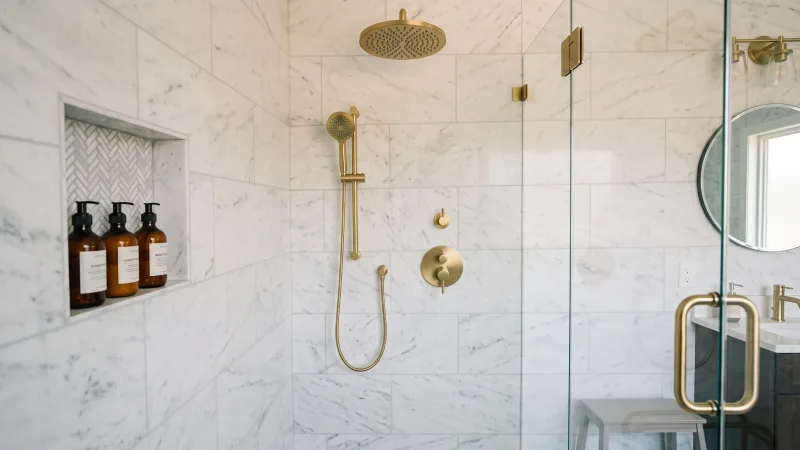 The interior of a walk-in shower with gold hardware and fixtures