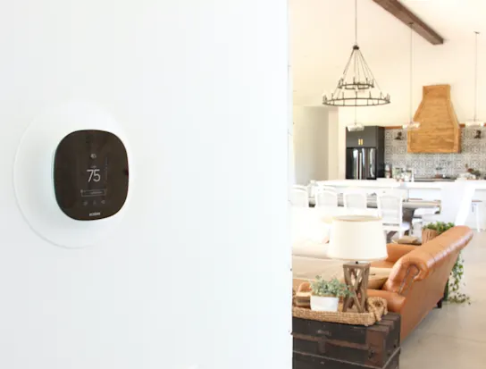 close up of a smart thermostat with a living room in the background