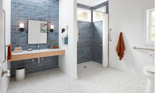 Large modern bathroom with blue tiled walls and accessibility bars; orange bath icon