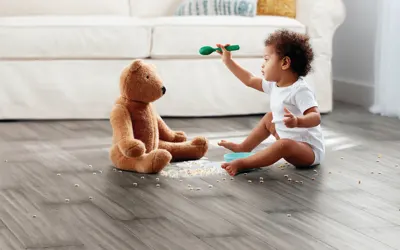 a baby sitting up playing with a teddy bear on new grey vinyl flooring