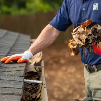 HD Service pro cleaning leaves out of the gutters of a home; orange checklist icon