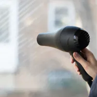 Someone weatherproofing their window using a blow dryer; orange snowflake icon