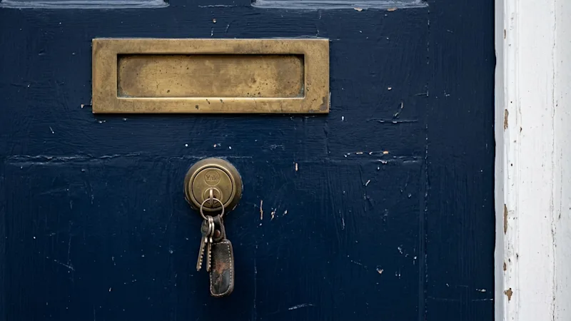 A navy blue front door on a British home, with a brass letterbox and a set of keys left in the lock