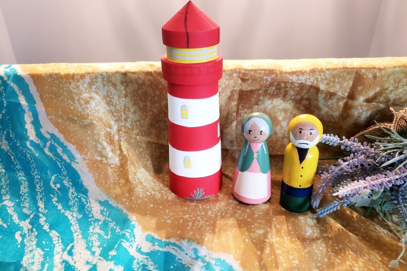 A lighthouse keeper and wife next to a lighthouse on a beach with foliage.