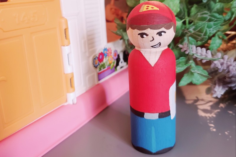 A pizza boy peg doll looking at the camera.