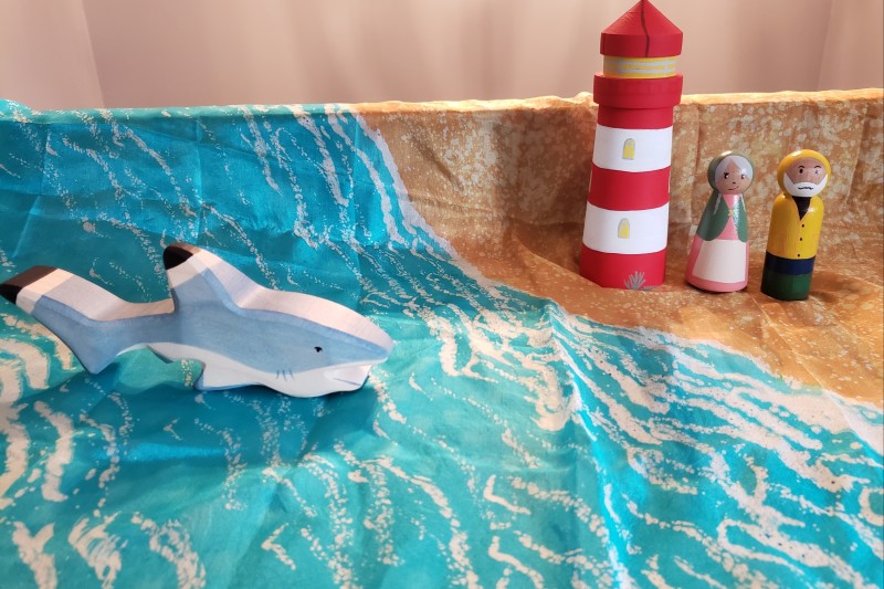 A lighthouse keeper and wife on a beach with a shark in the water.