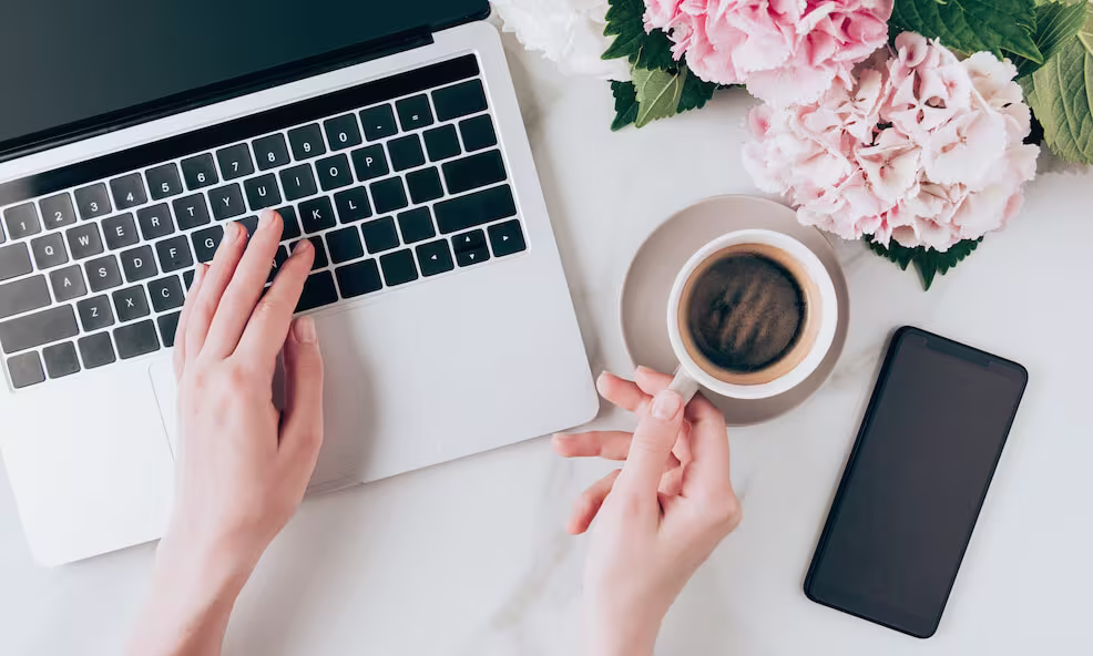 Pilt kätepaariast, kes kasutab sülearvutit ja hoiab kohvitassi