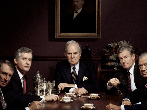 5 older men sitting at a table together, looking at camera