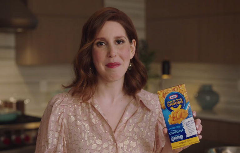 Vanessa Bayer holding up a Kraft Macaroni & Cheese box in a kitchen