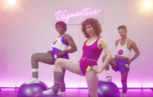 Three people holding rollers while placing their feet on exercise balls; a Vagnastics neon sign is in the background