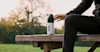 a man say on a bench outisde reaching for his huel shaker which is on the bench next to him