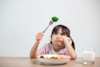 a child frowning at a piece of broccili on a fork with a plate of veg in front of them