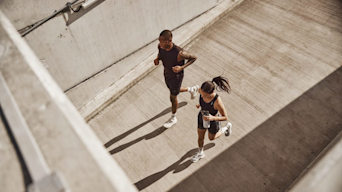 Man and woman running on concrete holding a Huel shaker