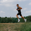 A man running through a grassy field with a treeline in the background