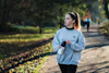 woman walking along a path in a park holding a huel shaker and looking off into hte distance