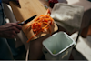 person scraping carrot peels off a chopping board into a bin