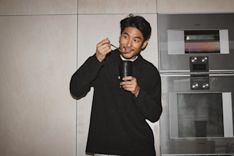 man stood in a kitchen eating huel hot and savoury from a huel pot