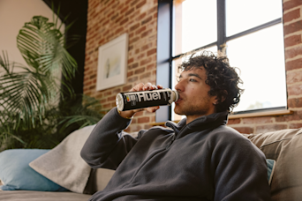 man sat on sofa drinking a huel vanilla black edition ready to drink