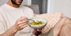 man sat on sofa eating huel hot and savoury from a bowl with a fork
