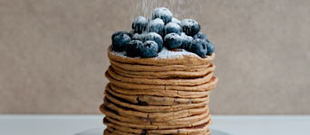 A stack of Huel Pancakes with Blueberries on top and powdered sugar