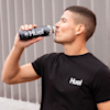 Marathon Runner Will Goodge wearing a black Huel t-shirt, drinking from a bottle of Huel Ready-to-drink