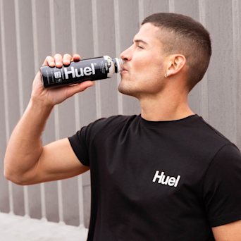Marathon Runner Will Goodge wearing a black Huel t-shirt, drinking from a bottle of Huel Ready-to-drink