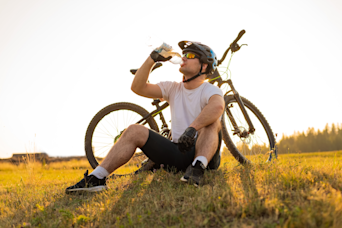 man sat on the grass drinking from his water bottle with his bicycle behind him