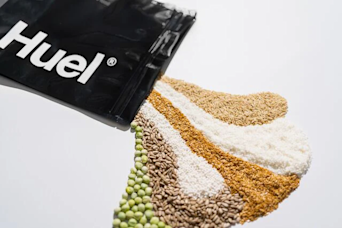 a bag of huel black edition lying flat with a variety of seeds and grains spilling out