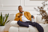 Man on a white couch, on his phone, holding a Huel shaker