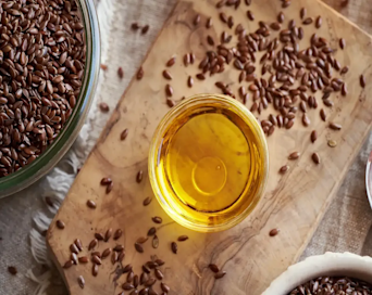 Flax seed oil in a small glass bowl next to loose flaxseeds