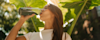 Woman drinking Huel Daily Greens against a plant backdrop