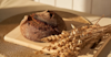 a freshly baked loaf of bread on a wooden board next to some raw wheat