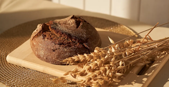 a freshly baked loaf of bread on a wooden board next to some raw wheat