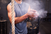 man chalking his hands in a gym with a climbing rope next to him